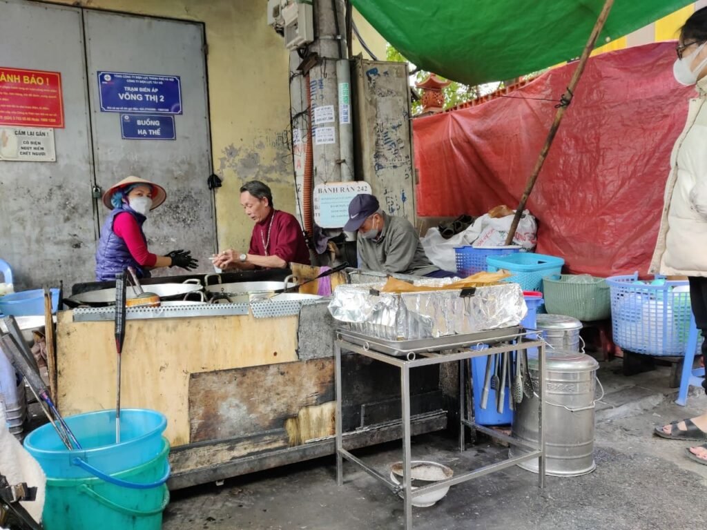 Photographie d'un restaurant de rue (street food) spécialisé dans les bánh rán mặn, un plat salé vietnamien, dans une intersection à Hanoi, au Vietnam